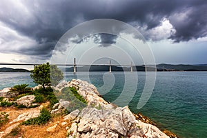 The bridge to the island of PeljaÅ¡ec and above it dramatic storm clouds of incoming storm fronts