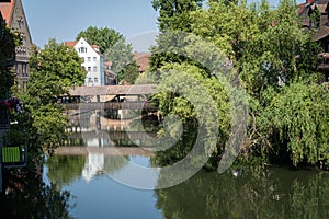 Bridge, trees, and buildings reflected on the Pegnitz river on a sunny day