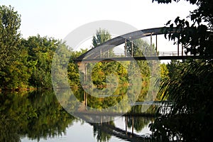 Bridge and trees reflecting at green river in summer