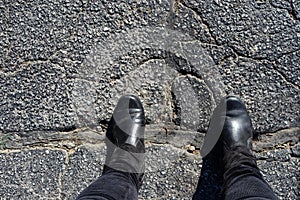 Bridging the Divide - Feet of woman in black boots stands with feet across big repair in cracked asphalt photo