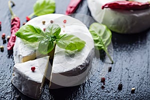 Brie cheese. Camembert cheese. Fresh Brie cheese and a slice on a granite board with basil leaves four colors peper and chili pepe