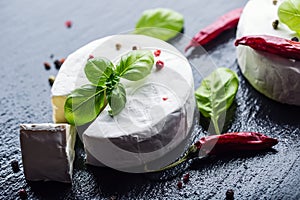 Brie cheese. Camembert cheese. Fresh Brie cheese and a slice on a granite board with basil leaves four colors peper and chili pepe