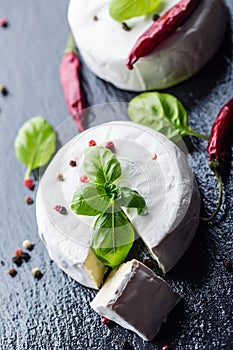 Brie cheese. Camembert cheese. Fresh Brie cheese and a slice on a granite board with basil leaves four colors peper and chili pepe