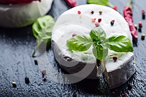 Brie cheese. Camembert cheese. Fresh Brie cheese and a slice on a granite board with basil leaves four colors peper and chili pepe