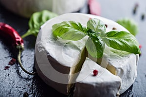 Brie cheese. Camembert cheese. Fresh Brie cheese and a slice on a granite board with basil leaves four colors peper and chili pepe