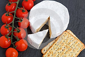 Brie soft cheese with crackers and tomato on a grey slate boar