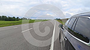 A brief stop during a summer road trip. The car is parked on the side of a paved highway with markings next to a grassy meadow and