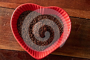 Brigadeiro over a red heart shaped bowl and wooden background photo