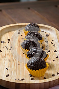 Brigadiers lined up on a wooden plate. The focus is on the brigadeiro in the center. photo