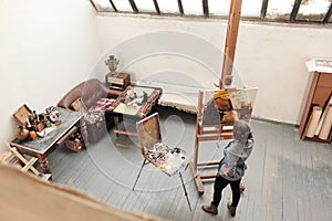 Bright art studio with a large window. Easels and canvases. Woman artist paints a picture on canvas.