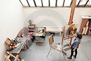 Bright art studio with a large window. Easels and canvases. Woman artist paints a picture on canvas.