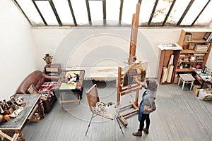 Bright art studio with a large window. Easels and canvases. Woman artist paints a picture on canvas.