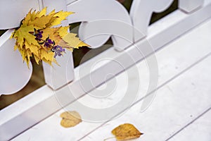 Bright autumn bouquet of fallen leaves and violet flower close-up in white bench in park, sunny day, autumn natural