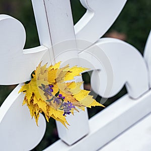 Bright autumn bouquet of yellow fallen leaves and violet flower close-up in white bench in park, sunny day, autumn