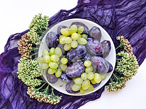Bright autumn composition of plums, grapes and wild flowers on a plate. Flat lay, top view