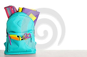 Bright backpack with school stationery on stone table against white background