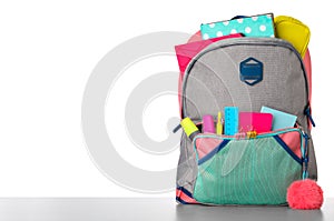 Bright backpack with school stationery on stone table against white background