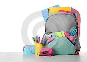 Bright backpack with school stationery on stone table against white background