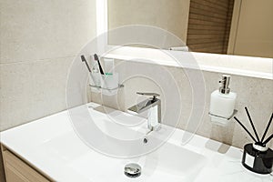 Bright bathroom interior with white sink and toothbrushes, flavoring and liquid soap on it