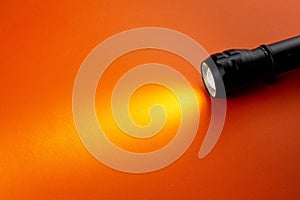 A bright beam of light from a flashlight shines on an orange background, Halloween theme copy space