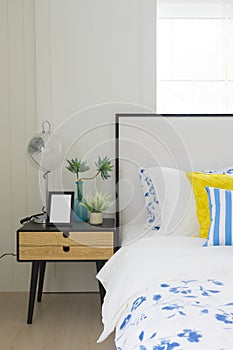 Bedroom interior with striped pillow on bed and bedside table lamp with picture frame on it.