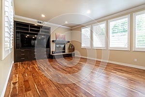 Bright beige large empty room with wood floor, molding and windows.