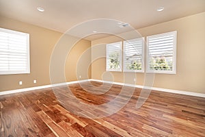 Bright beige large empty room with wood floor, molding and windows.