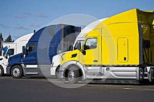 Bright big rig semi trucks standing in row on truck stop in sunny day