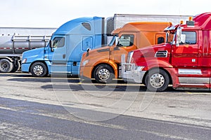 Bright big rigs semi trucks standing in row on truck stop