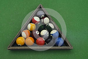 Bright billiard balls and a cue ball for billiards, in a wooden triangle on the playing table. Next to the cue stick. Preparation