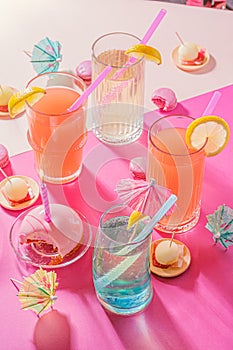 Bright birthday party background with cocktails and candy. Colored holiday accessories on pink table. Top view