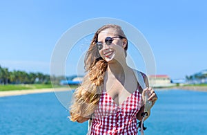 Bright blond young woman standing with backpack near sea in summer