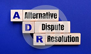 On a bright blue background, light wooden blocks and cubes with the text ADR Alternative Dispute Resolution