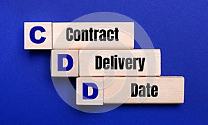 On a bright blue background, light wooden blocks and cubes with the text CDD Contract Delivery Date