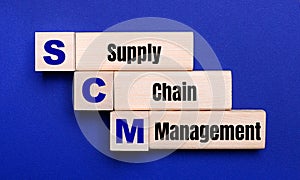 On a bright blue background, light wooden blocks and cubes with the text SCM Supply Chain Management