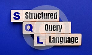 On a bright blue background, light wooden blocks and cubes with the text SQL Structured Query Language