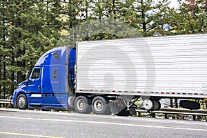 Bright blue big rig high cab semi truck transporting cargo in refrigerated semi trailer driving on the highway road