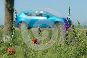 Bright blue car and spring flowers on the foreground. Road trip concept.