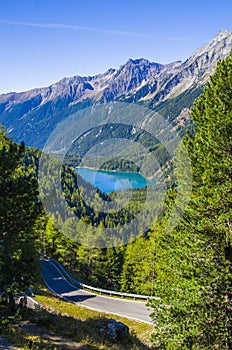 Bright blue mountain lake under blue sky with woods, stones and snow