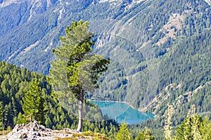 Bright blue mountain lake under blue sky with woods, stones and snow