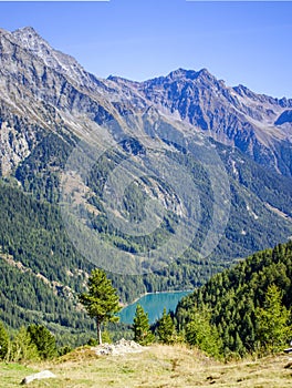 Bright blue mountain lake under blue sky with woods, stones and snow