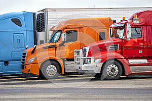 Bright blue orange and red big rig semi trucks standing on row on the truck stop waiting for continue delivery