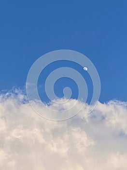 Bright blue sky with fluffy white clouds and the moon in the daytime. Beautiful and serene natural view capturing