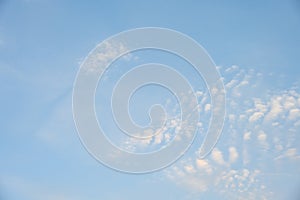 Bright blue sky with pale yellow tinged puffy white clouds, as a nature background