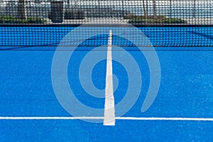 Bright blue tennis, paddle ball or pickleball court ground view with white line towards black net outdoors