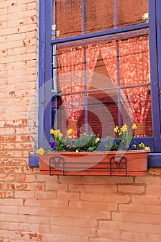Bright blue window with flowers and colorful curtains in red brick wall