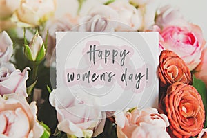 bright bouquet of colorful roses with white card with the inscription happy women s day  concept of congratulations on