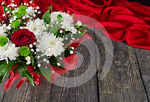 Bright bouquet of roses and white chrysanthemums on wooden background and scarlet fabric