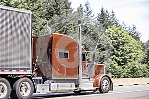 Bright brown classic American big rig semi truck with vertical chrome pipes transporting cargo in aluminum refrigerator semi