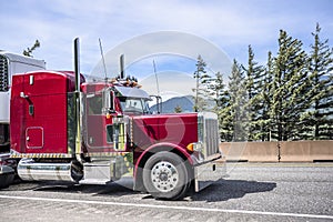 Bright burgundy classic bonnet American big rig semi truck with stylish chrome parts transporting cargo in refrigerator semi
